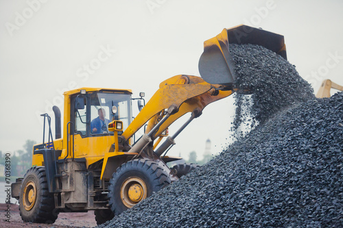 Yellow heavy excavator and bulldozer unloading road metal during photo