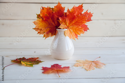 Autumn maple leaves bunch in vase on old wooden background