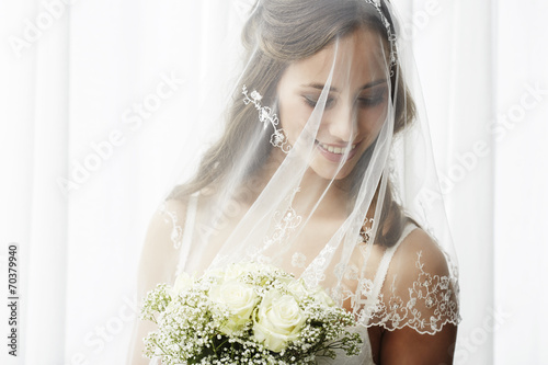 Excited young bride in veil holding bouquet. photo