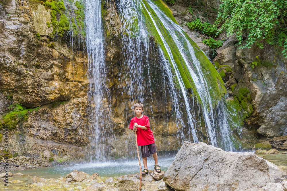young happy smiling child boy on waterfall background