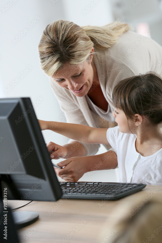 Teacher with little girl in class using computer and tablet