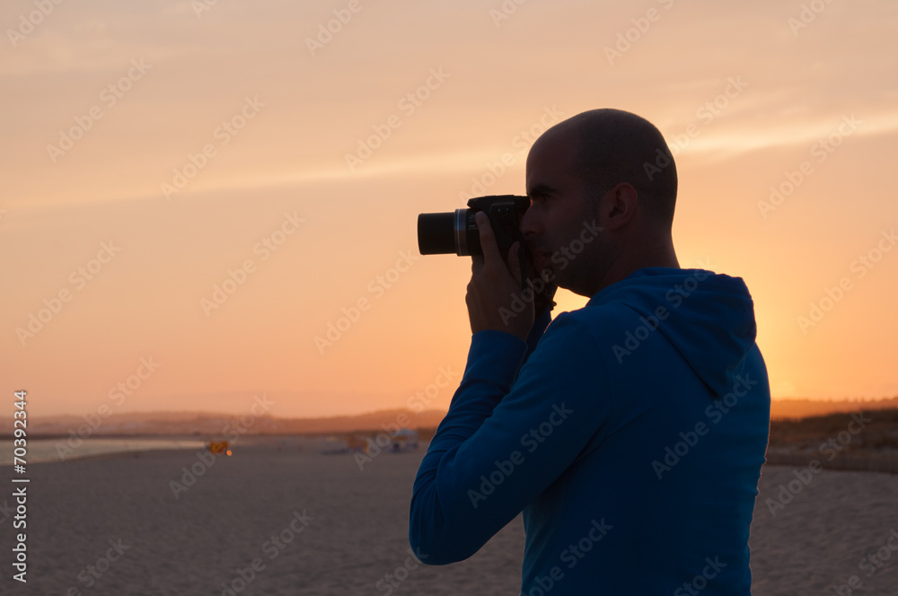 Young man taking photos in the beach at sunset