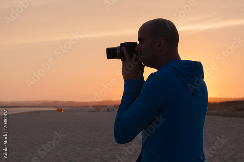 Young man taking photos in the beach at sunset