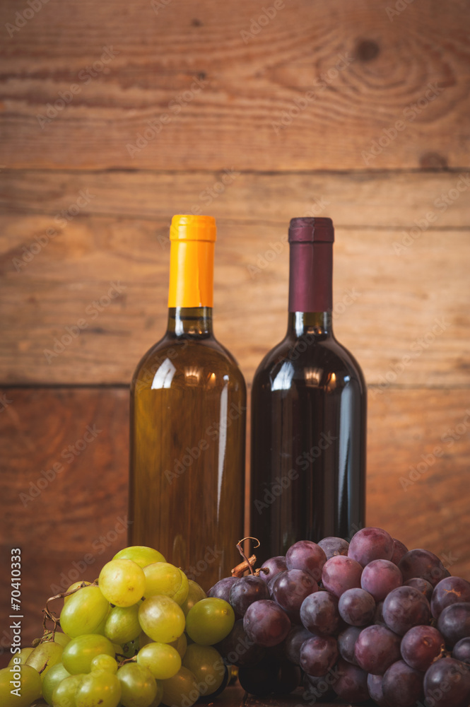Red and white wine bottle with grapes on wooden rustic table.
