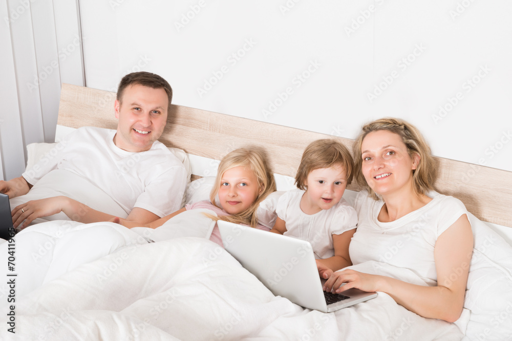 Young Family Using Laptops In Bed