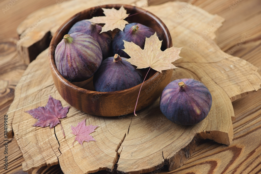 Wooden bowl with figs and maple leaves, rustic wooden background