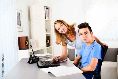 cheerful young teacher helping a teenager doing homework