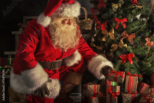 Fotografie, Obraz Santa is placing gift boxes under Christmas tree
