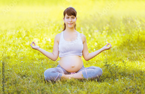 Happy pregnant woman yoga outdoors on the grass
