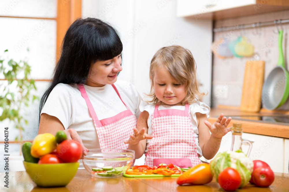 mother teaching kid daughter preparing salad at kitchen