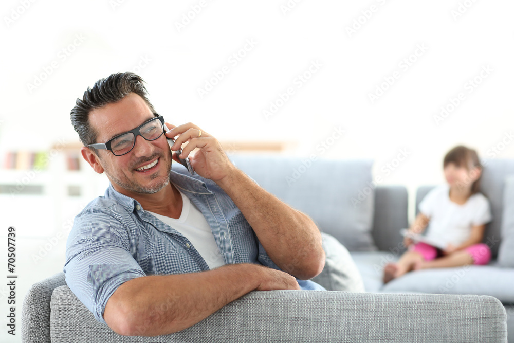 Man in sofa talking on phone, girl in background