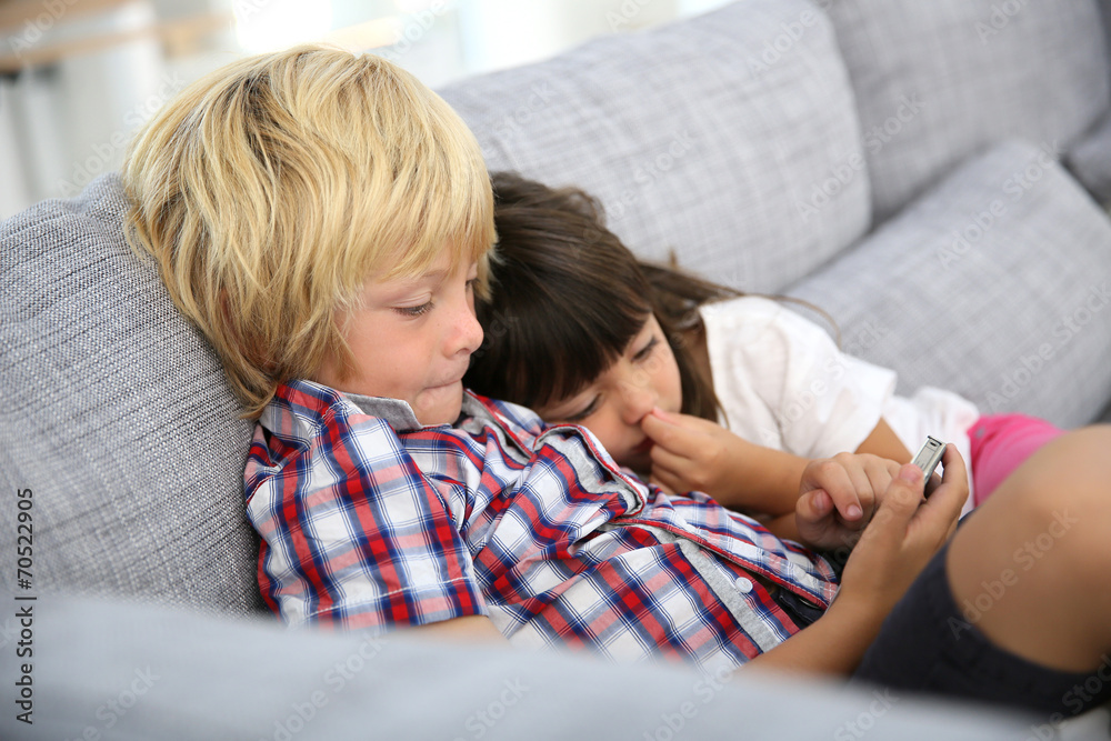 Fototapeta premium Kids sitting in sofa and playing with smartphone