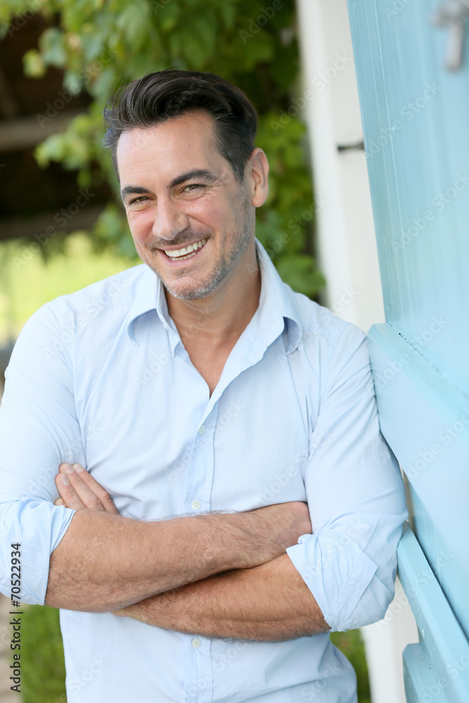 Fototapeta premium Smiling 40-year-old man leaning on home wall