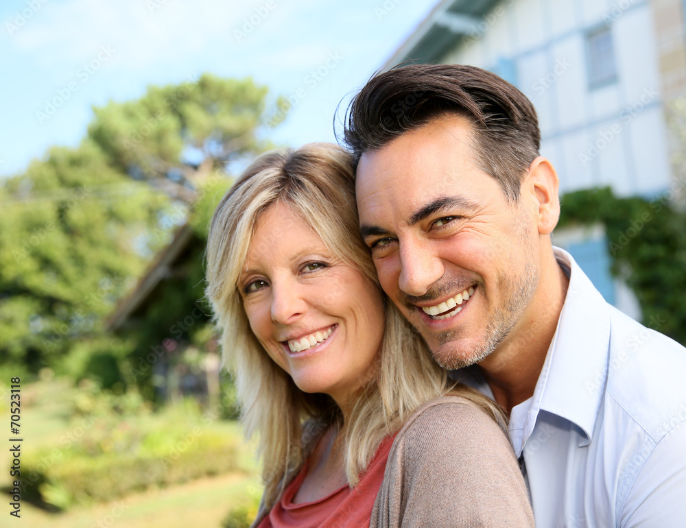 Cheerful mature couple standing in front of house Cheerful mature couple standing in front of house
