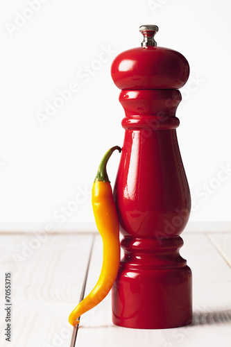 Gelbe Peperoni, rote Pfeffermühle auf weissem Holztisch