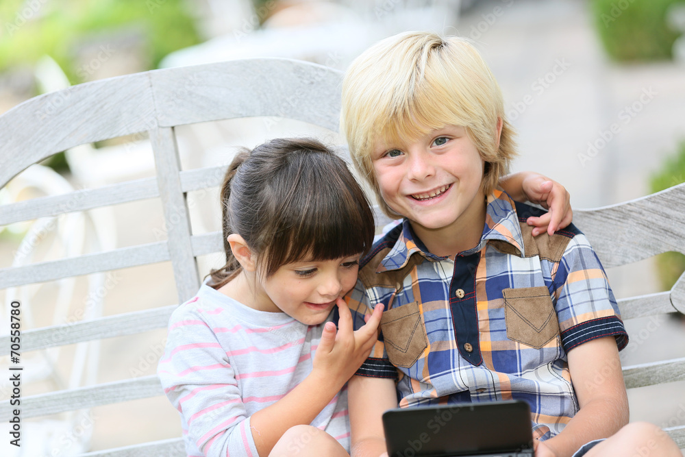 Kids sitting on outdoor bench and playing video games Kids sitting on outdoor bench and playing video games