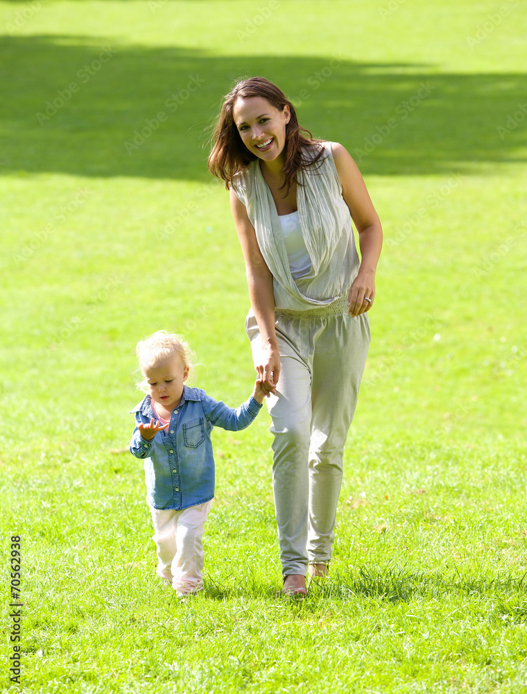 Fototapeta premium Smiling mother and daughter walking on grass
