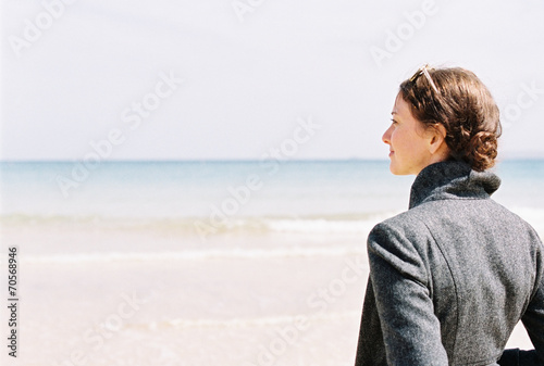 A woman in a grey jacket looking out over a beach and the sea.