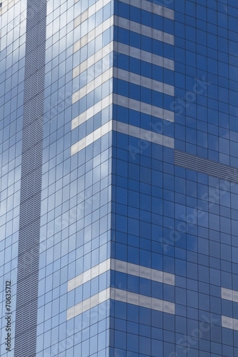 Glass skyscraper with blue sky and clouds reflected in windows.