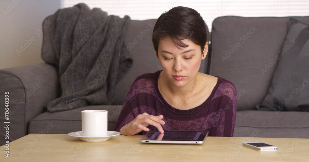 Asian woman sitting at coffee table with tablet Asian woman sitting at coffee table with tablet
