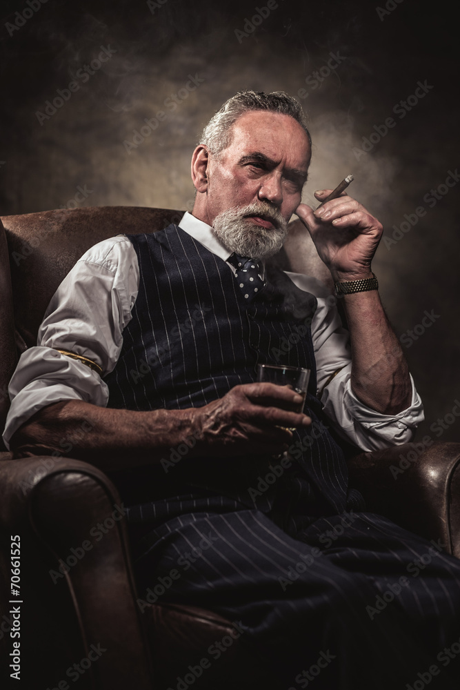 In chair sitting senior business man with cigar and whisky. Gray