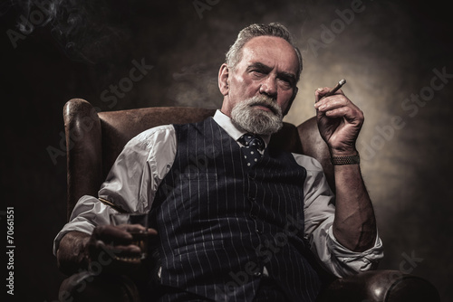 In chair sitting senior business man with cigar and whisky. Gray