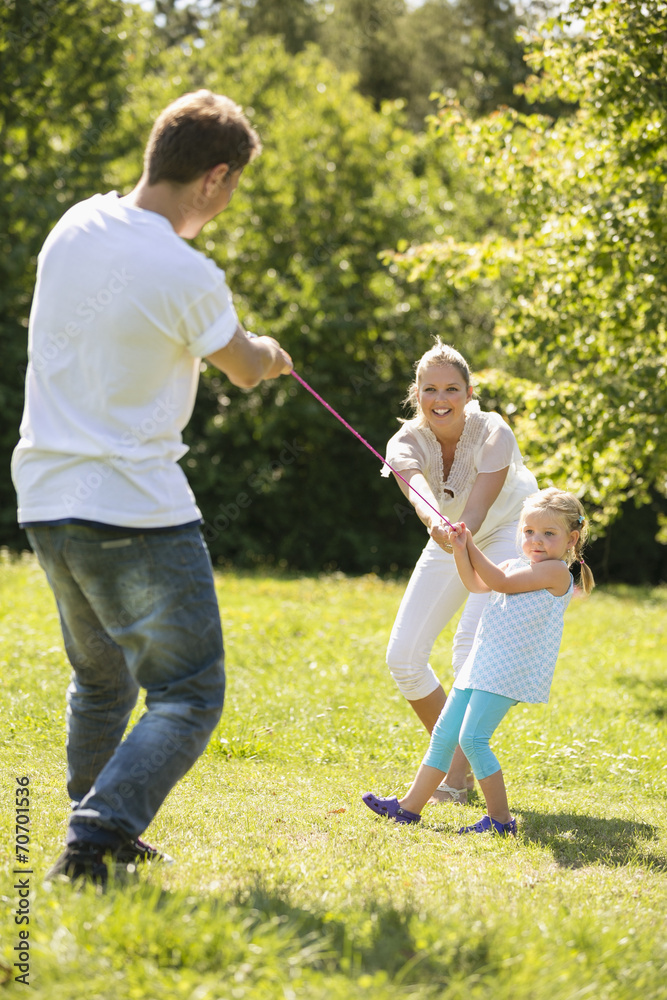 Fototapeta premium Junge Familie spielen Seilziehen im Garten