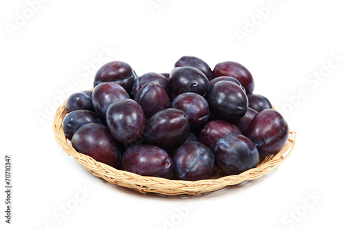 Fresh plums in a wooden basket on white background.