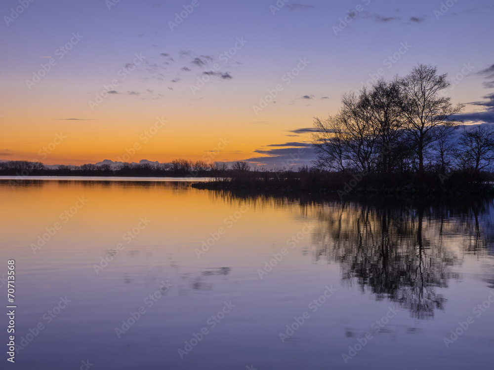 Fototapeta premium Trees and Clouds reflecting in a lake during a beautiful Sunset