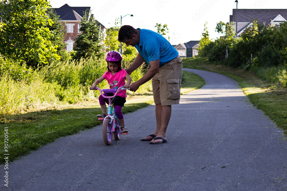 Obraz premium Little girl learning how to ride a bike with her dad