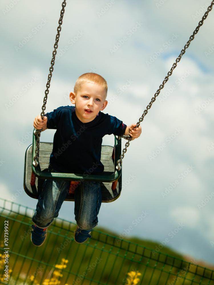 Little blonde boy child having fun on a swing outdoor