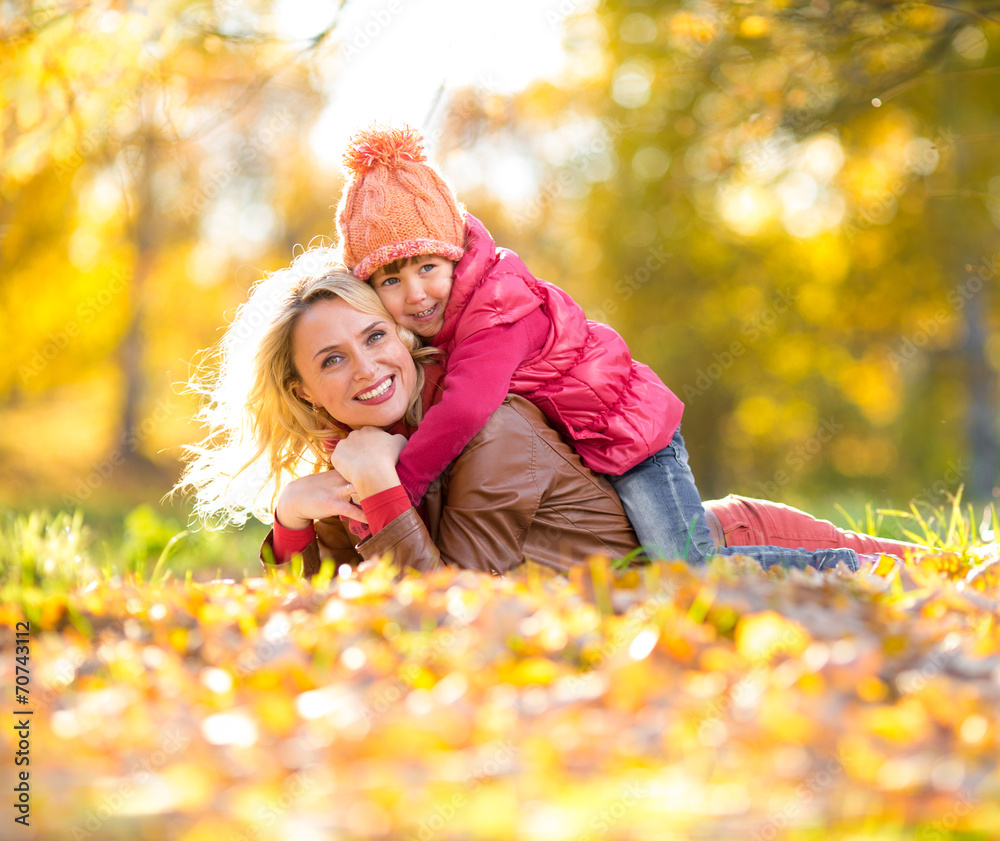 Parent and kid lying together on falling leaves. Happy family ou Parent and kid lying together on falling leaves. Happy family ou