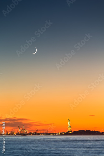 Statue of Liberty under a rising new moon at sunset