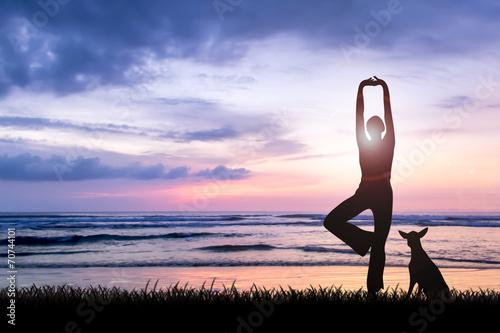 Silhouette of young woman practising yoga on beach at sunset