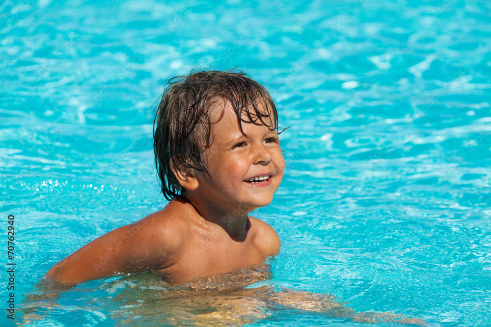 Smiling boy swimming in pool and looking