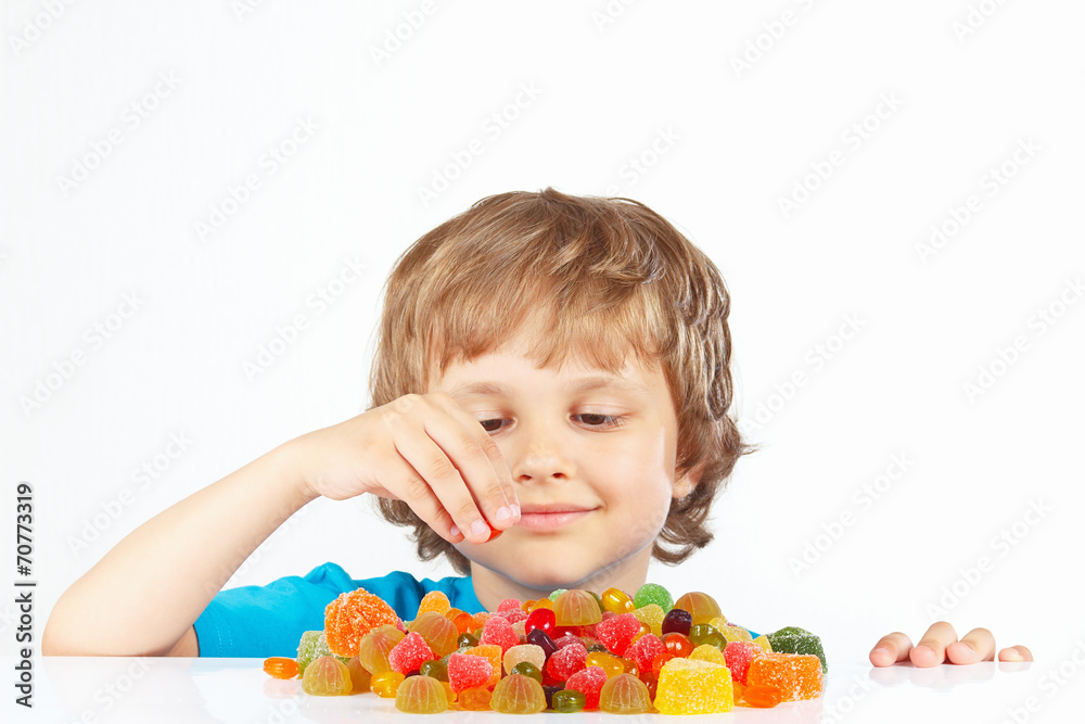 Little blonde boy with candies on a white background