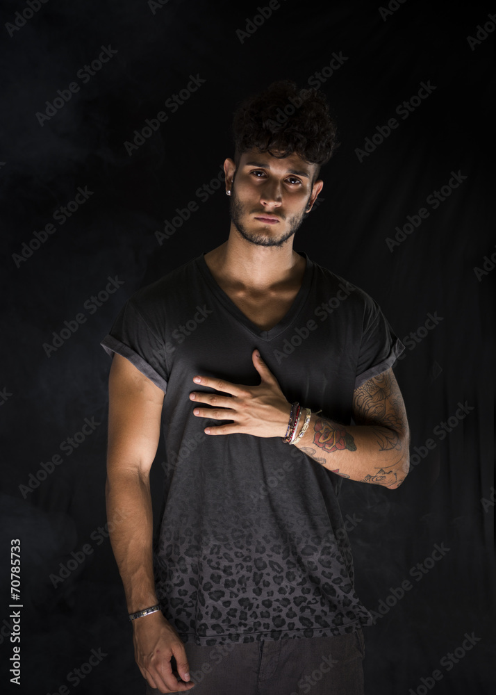 Portrait of handsome young man in dark t-shirt on black