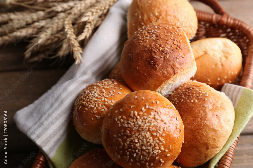 Tasty buns with sesame in wicker basket, on wooden background Tasty buns with sesame in wicker basket, on wooden background