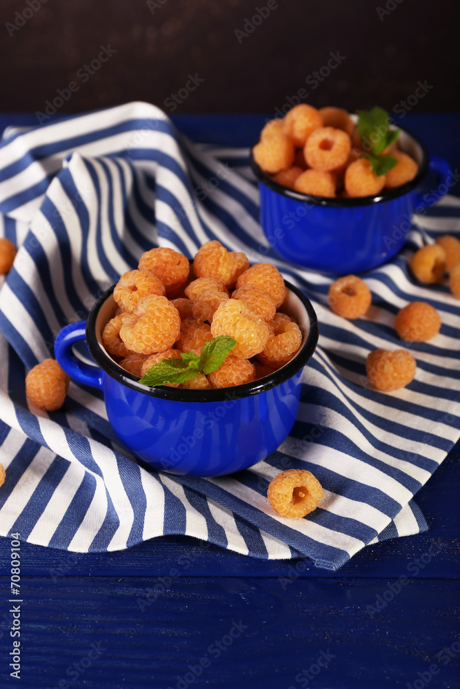 Yellow raspberries in dark blue mugs