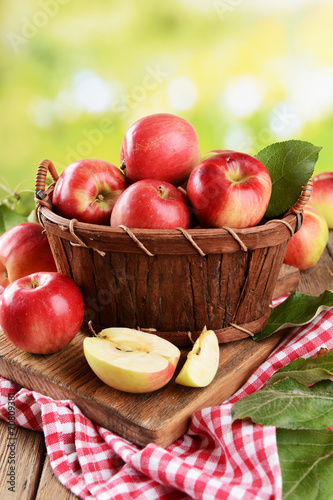 Sweet apples in wooden basket on table on bright background