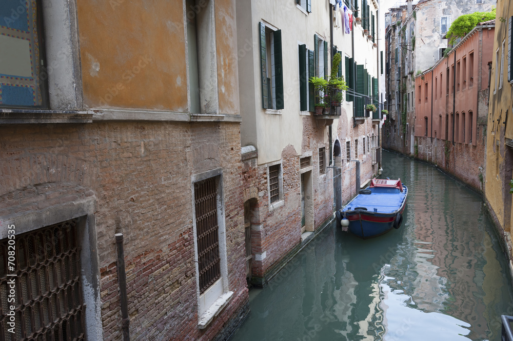 Narrow canal among old brick houses in Venice, Italy.