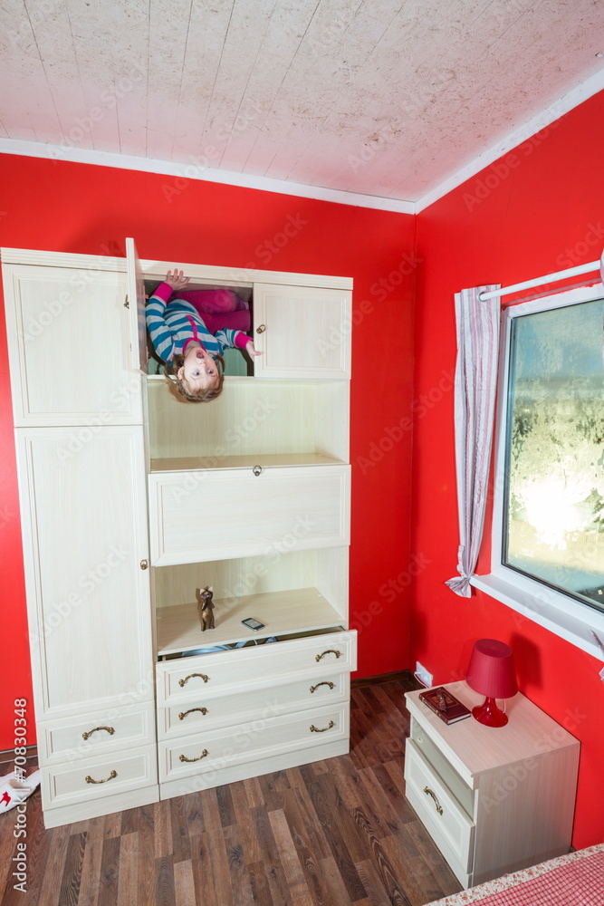 Fototapeta premium Little girl upside down in open closet at inverted house