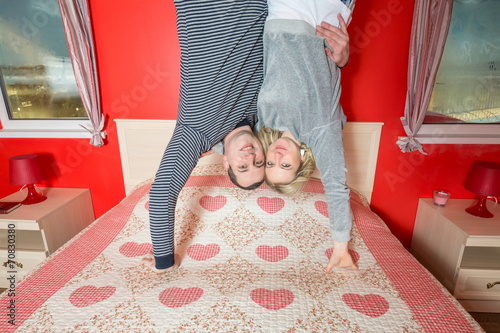 Couple in an embrace stand upside down on bed in bedroom photo