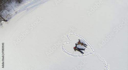 Aerial view to man and girl lying on snow inside the heart photo