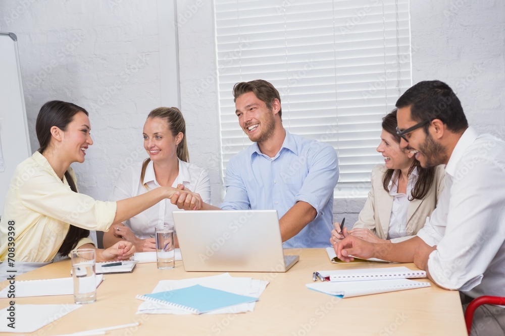 Casual business people shaking hands at desk and smiling Casual business people shaking hands at desk and smiling