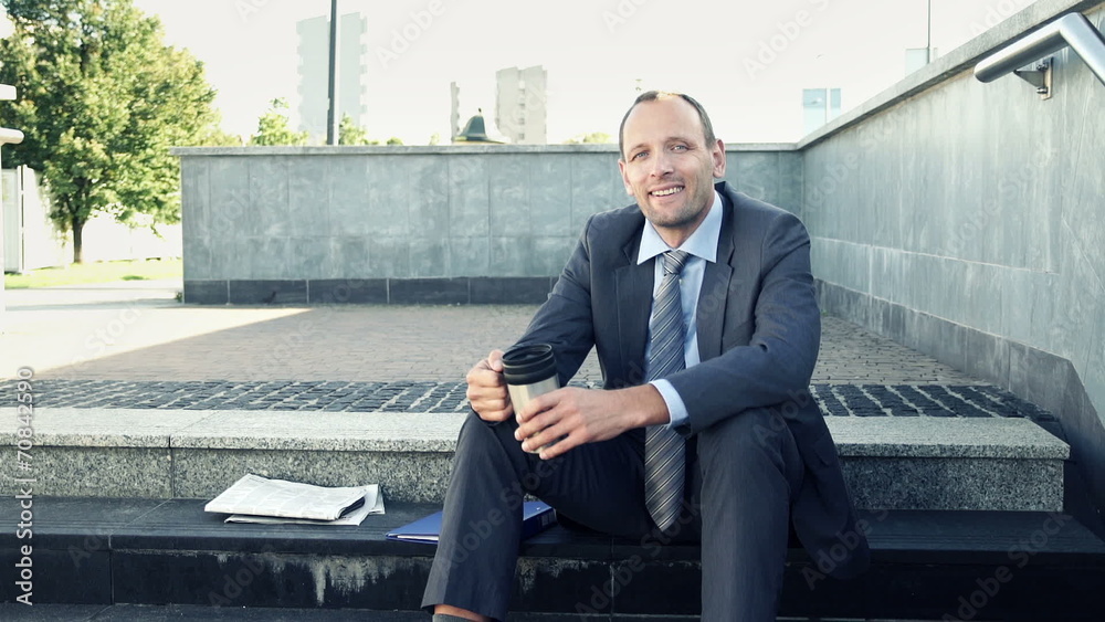 Portrait of young happy businessman drinking coffee on stairs in Portrait of young happy businessman drinking coffee on stairs in