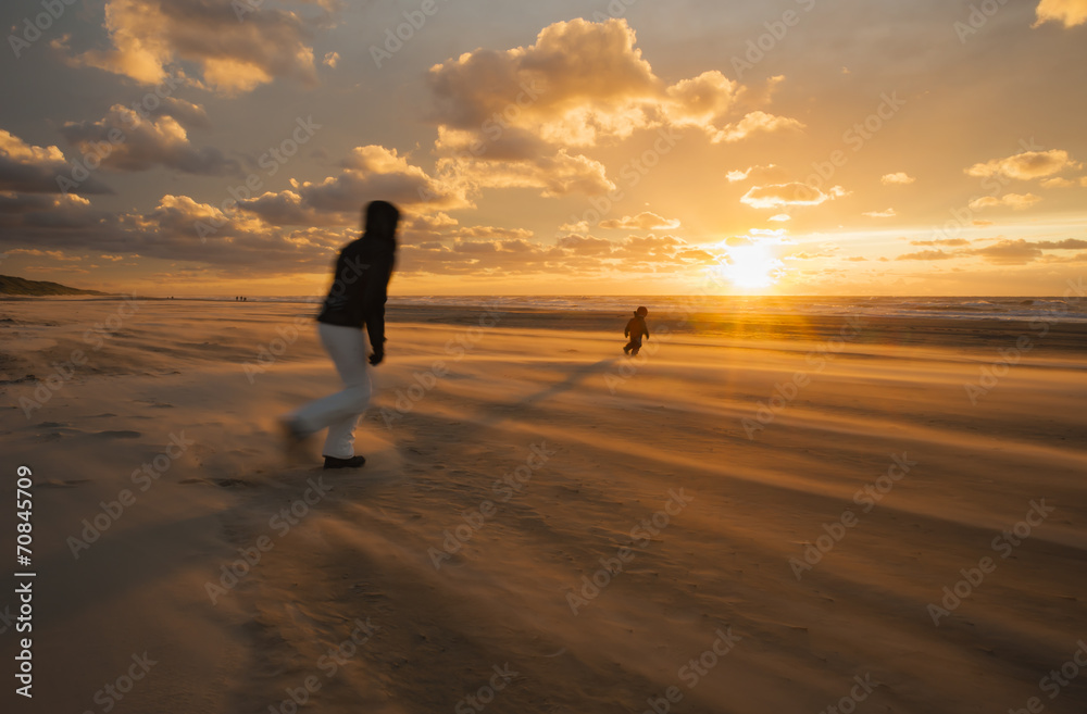 Denmark, Jutland, Lokken, mother trying to catch her child on stormy beach at sunset Denmark, Jutland, Lokken, mother trying to catch her child on stormy beach at sunset