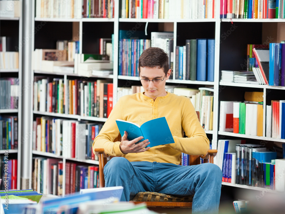 Young man sitting in a library reading a book Young man sitting in a library reading a book