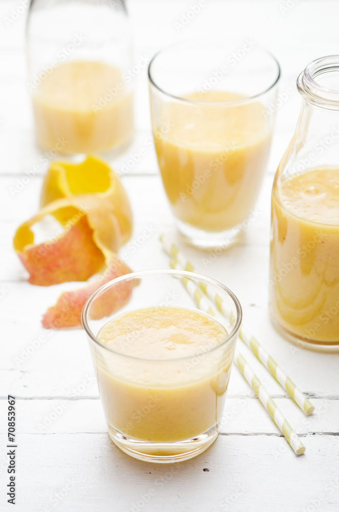 Glasses and bottles of mango banana smoothie on white wooden table Glasses and bottles of mango banana smoothie on white wooden table