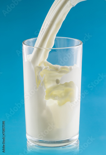 Milk is pouring into the glass on blue background